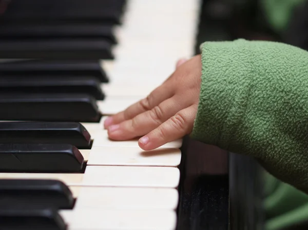 Детская рука в зеленом рукаве играет на пианино — стоковое фото