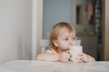 Komik küçük kız mutfakta oturmuş süt içiyor.