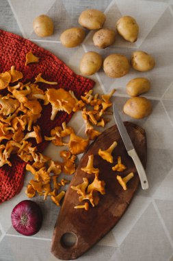 Taze mantarlar, patatesler ve soğan ahşap kesim tahtasının üzerinde.
