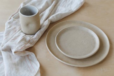 Ahşap masa manzaralı bej seramik tabak. Minimalist el yapımı seramik sofra takımı ve çömlek.