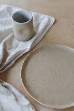 Ahşap masa manzaralı bej seramik tabak. Minimalist el yapımı seramik sofra takımı ve çömlek.