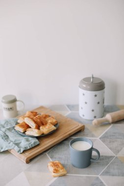 Mutfak masasında yeni pişmiş ev yapımı hamur işi. Kahvaltıda poğaça ve bir bardak süt.