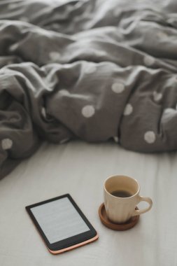 E-kitap ve yatakta çarşafların üzerinde bir fincan kahve. İyi sabahlar. Yatakta kahvaltı.