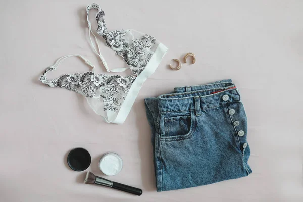 Composición laica plana con ropa interior femenina, sujetador, jeans, cosméticos y accesorios sobre fondo beige vista superior —  Fotos de Stock