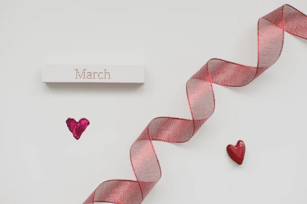 Červená stuha a červené srdce na bílém pozadí. 8. března, koncept Mezinárodního dne žen. — Stock fotografie