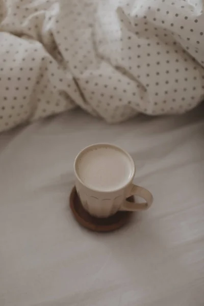 Beyaz çarşaflı ve battaniyeli bir fincan sütlü kahve. Yatak konseptinde sabah kahvesi. — Stok fotoğraf