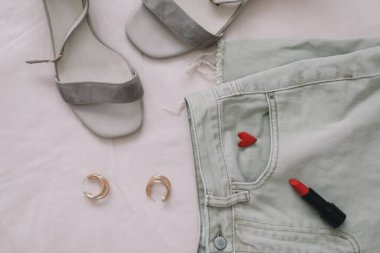 Bej arka planda kot pantolon, sandalet ve kırmızı ruj. Kadınların yaz giysisinin genel görünüşü. Moda tarzı kadın kıyafetleri. Düz yatış, üst görünüm