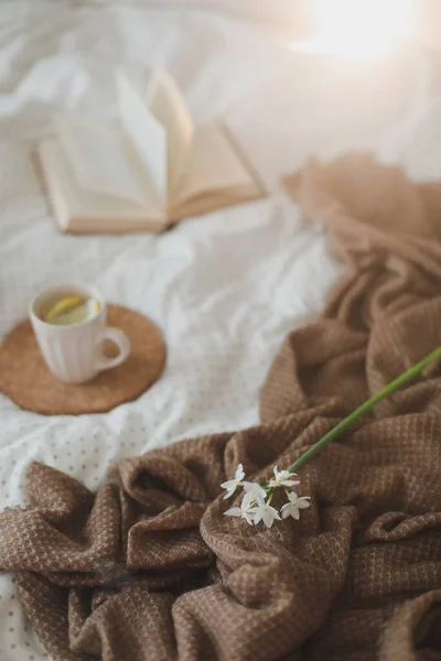 Cup of lemon tea, daffodil flower and a book on bed. Breakfast in bed. Morning. Spring. — Stock Photo, Image