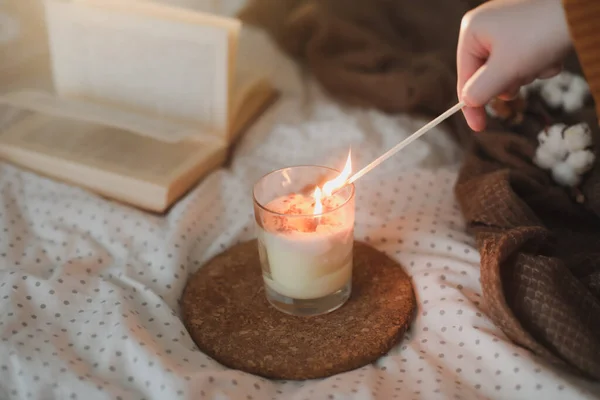 Tangan menyalakan lilin dengan korek api. Nyaman masih hidup interior rincian dengan buku, lilin om kotak-kotak. Sweet rumah Stok Gambar