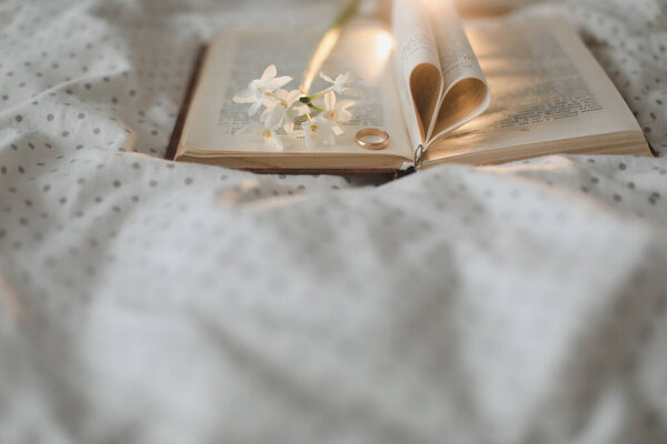 Golden ring and open book with folded sheets in heart shape in bed. Wedding concept, Happy Valentines Day.