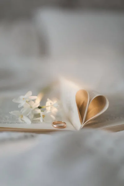 Zlatý prsten a otevřená kniha se složenými prostěradly ve tvaru srdce v posteli. Svatební koncept, Šťastný Valentýn — Stock fotografie