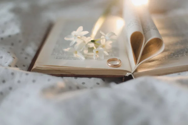 Anillo dorado y libro abierto con sábanas plegadas en forma de corazón en la cama. Concepto de boda, Feliz día de San Valentín — Foto de Stock