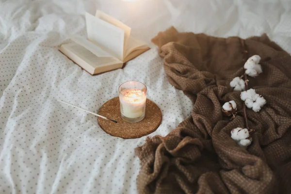 Detalles interiores de naturaleza muerta acogedores con un libro, una vela y una ramita de algodón en una cama suave y cálida. Dulce hogar — Foto de Stock