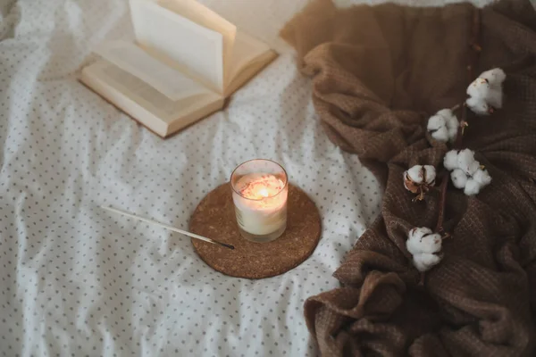 Detalles interiores de naturaleza muerta acogedores con un libro, una vela y una ramita de algodón en una cama suave y cálida. Dulce hogar — Foto de Stock