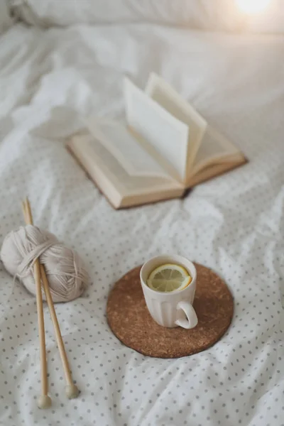 Bir kitap, çay fincanı ve sıcak, yumuşak bir yatakta örgü iğneleriyle hayat dolu detaylar. Güzel ev. — Stok fotoğraf
