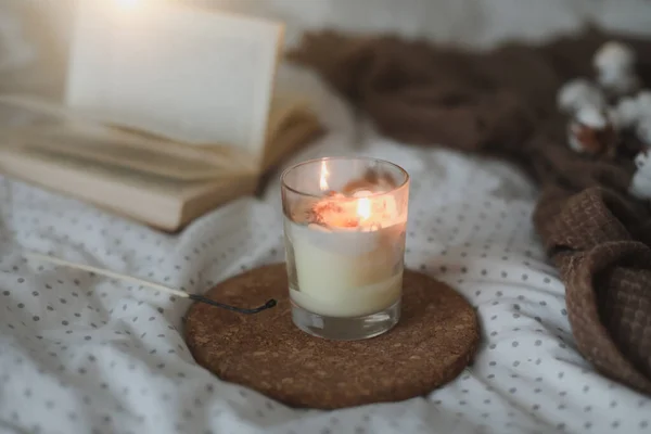 Accoglienti dettagli interni di nature morte con un libro, una candela e un ramoscello di cotone in caldo letto morbido. Dolce casa — Foto Stock