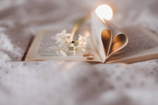 Golden ring and open book with folded sheets in heart shape. Wedding concept, Valentines Day.