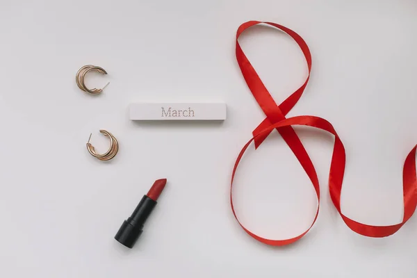 Ocho de ribbom rojo, lápiz labial y accesorios planas vista superior. Concepto Día de la Mujer, 8 de marzo — Foto de Stock