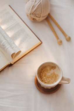 Bir kahve fincanı, iğneler ve yatakta kalp şeklinde katlanmış sayfalarla dolu bir kitapla sakin bir sabah.
