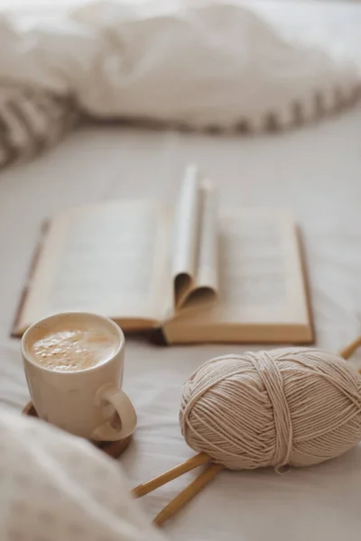 Cozy morning still life with a coffee cup, needles and a book with pages folded into a heart shape in bed — Stock Photo, Image