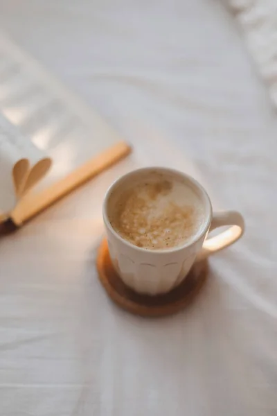 Composição de manhã acolhedora com uma xícara de café e um livro com páginas dobradas em forma de coração na cama — Fotografia de Stock