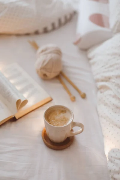 Nature morte du matin confortable avec une tasse à café, des aiguilles et un livre avec des pages pliées en forme de coeur dans le lit — Photo
