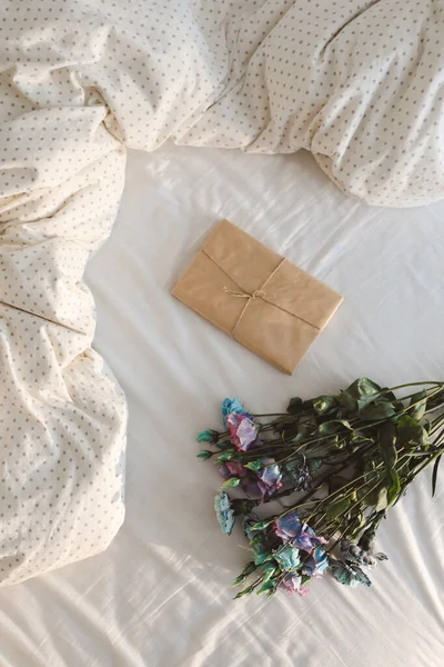 花の花束とギフト紙に覆われた砕いた白いベッドのシーツ ストックフォト