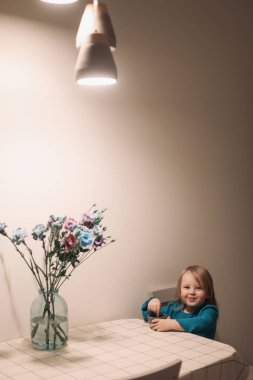 Komik, gülümseyen küçük bir kız yemek yiyor ve masada oturuyor, aile hayatı tarzı.