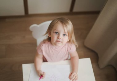 Masaya kalemlerle resim çizen küçük şirin bir kız. 