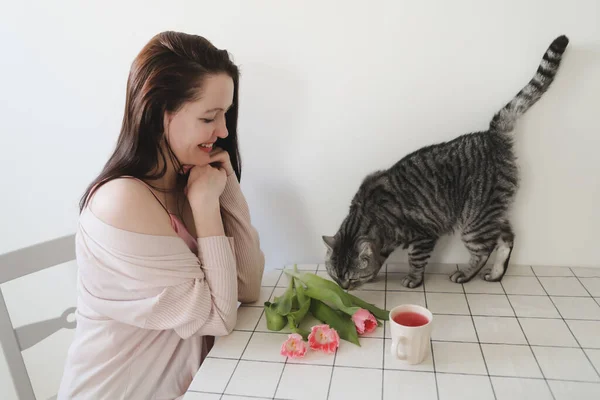 幸せな女性と彼女の猫匂い新鮮なピンクチューリップで朝に自宅で ロイヤリティフリーのストック画像