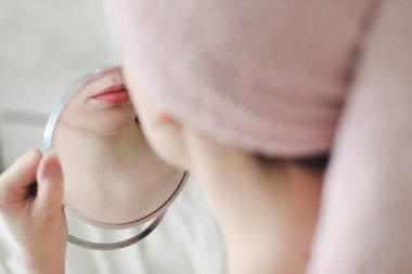 Güzel, çekici, gülümseyen bir kadın sabah makyajı sırasında küçük yuvarlak bir ayna kullanarak dudaklarını kırmızı rujla boyuyor..