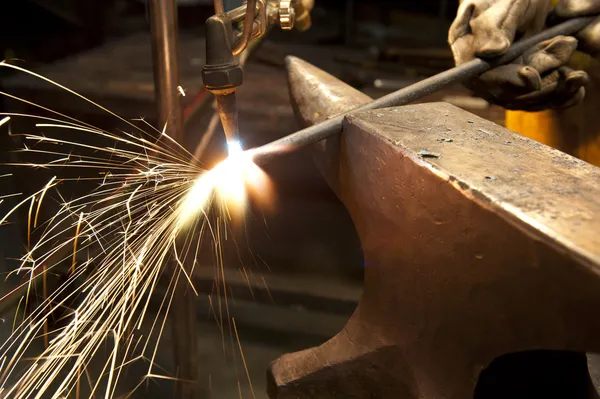 Kov továrník s využitím pochodeň ohřát kus kovu — Stock fotografie