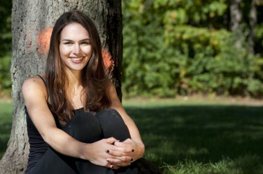 Bir ağacın yanında oturan genç esmer kız