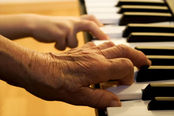 Hands of old piano player and grandchild — Stock Photo, Image