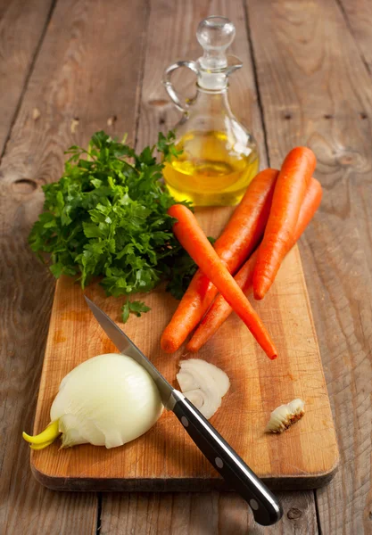 Cebolla, zanahorias y perejil fresco en una tabla de cortar . — Foto de Stock