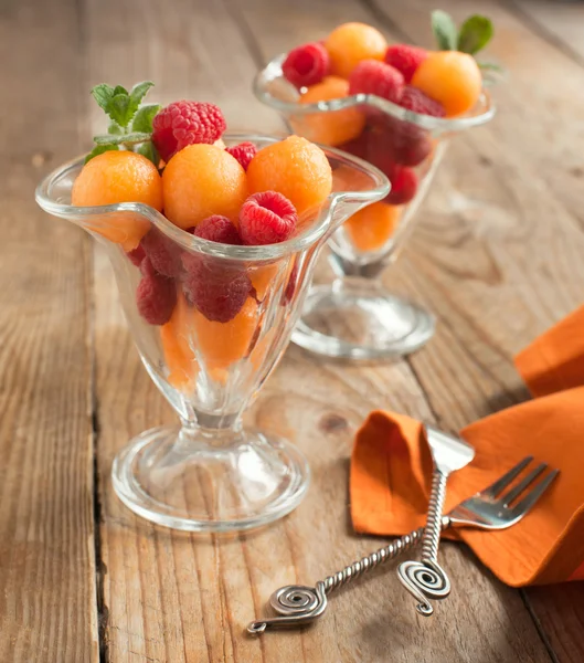 Fruit salad with melon balls and raspberries in glass bowl — Stock Photo, Image