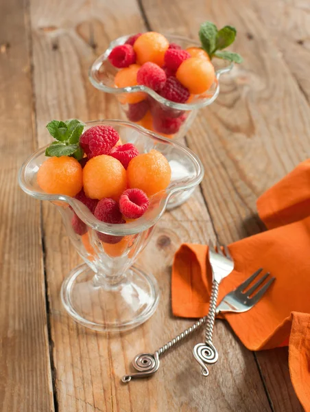 Fruit salad with melon balls and raspberries in glass bowl — Stock Photo, Image