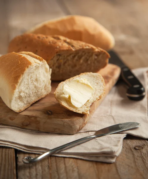 Pão de grão inteiro e pão branco em tábua de corte de madeira . — Fotografia de Stock