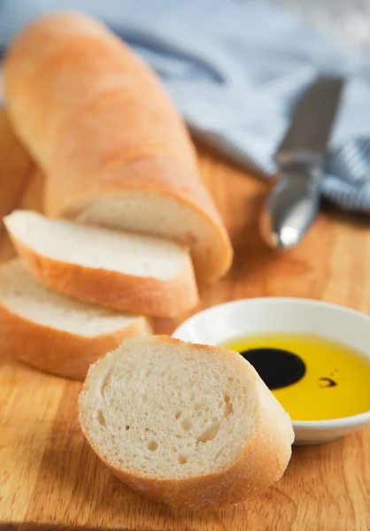 Baguete de pão francês cortada em tábua de pão de madeira e azeite . — Fotografia de Stock