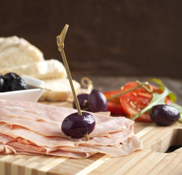 Нарезанная мортаделла на деревянной доске с хлебом, помидорами и оливками — стоковое фото
