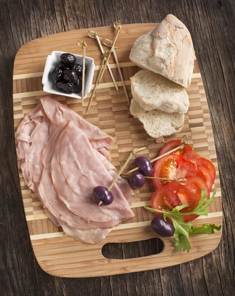 Нарезанная мортаделла на деревянной доске с хлебом, помидорами и оливками — стоковое фото