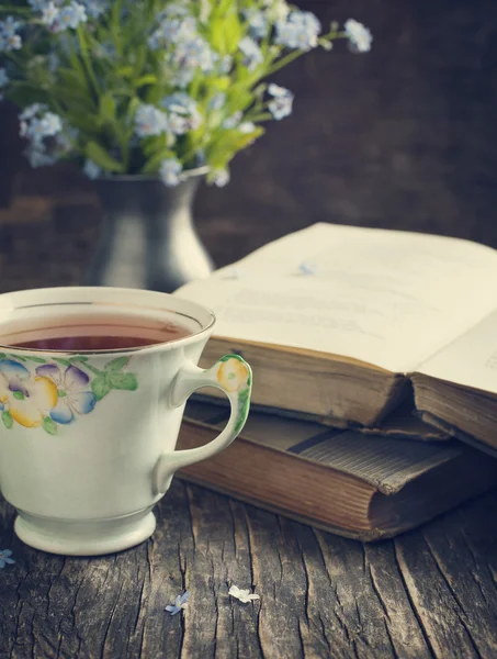 Taza de té, libros antiguos y flores azules de verano sobre la mesa . — Foto de Stock