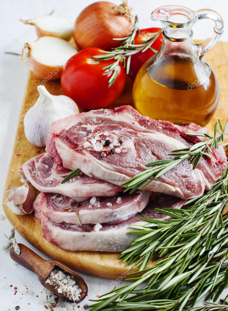 Raw lamb cutlets with vegetables, herbs and spices on wooden chopping board