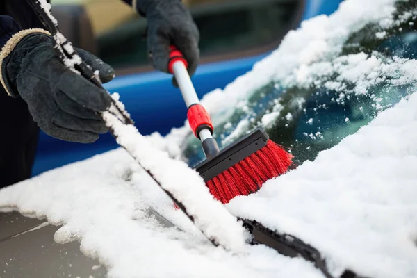 man in gloves lifting windscreen wiper with one hand and brushing off snow with other. Concept of removing ice and frost from a vehicle before drive in wintertime.