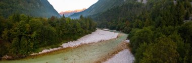 Panoramic horizontal composition of mountains and river in summer nature. Stream of water flowing through a ravine with green woodland around. Drone shot of Alps.
