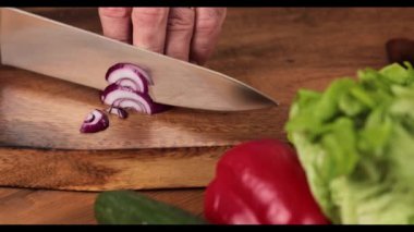 Erkek eli kesme tahtasındaki kırmızı soğanı kesiyor.