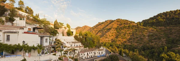 Panoramic photo overviewing the district of Sacromonte at sunset. White houses. Mountains with trees. Blue cloudy sky. Granada. Andalusia. Spain. — Stock Photo, Image