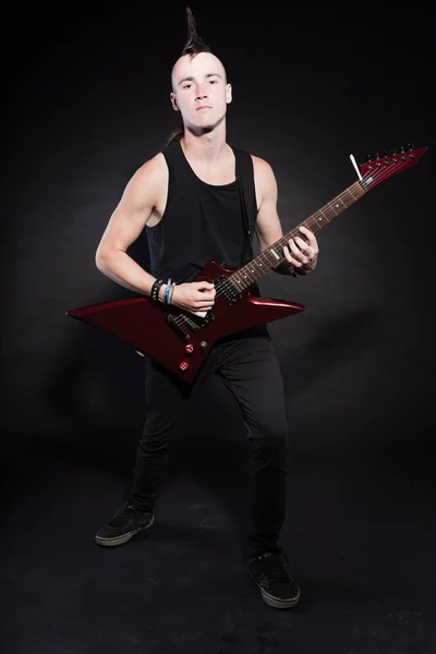 Punk rock homem com guitarra elétrica vermelha e corte de cabelo mohawk. Cara expressiva. Isolado em fundo preto. Estúdio . — Fotografia de Stock