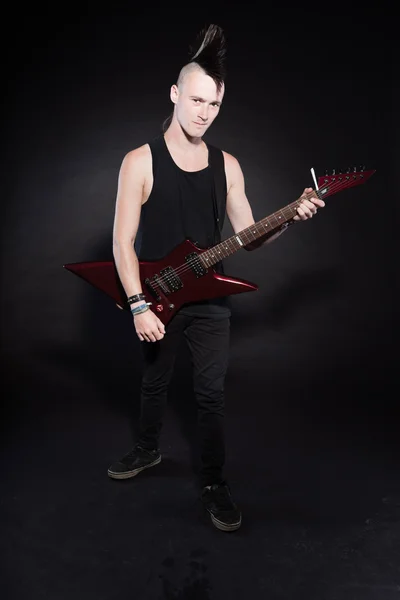 Πανκ ροκ άνθρωπος με κόκκινο ηλεκτρική κιθάρα και mohawk κούρεμα. εκφραστικό πρόσωπο. απομονώνονται σε μαύρο φόντο. Studio που γυρίστηκε. — Φωτογραφία Αρχείου