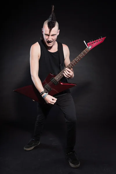 Punk rock hombre con guitarra eléctrica roja y corte de pelo mohawk. Cara expresiva. Aislado sobre fondo negro. Captura de estudio . —  Fotos de Stock